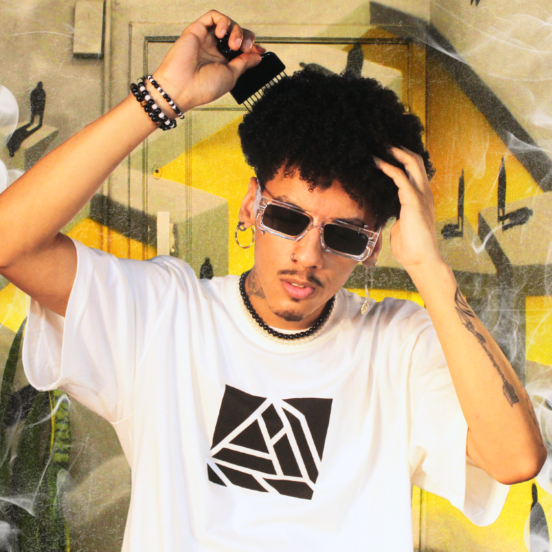 Um rapaz de óculos escuro, com um cableo afro e com um pente na mão, usando uma camiseta da Vents com o logo no meio da Vents