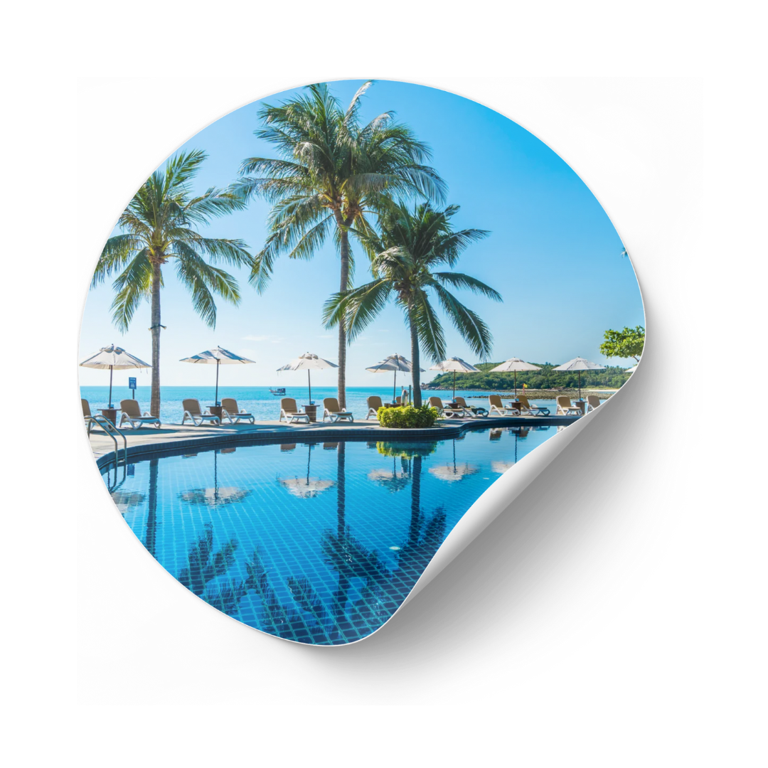Cena à beira da piscina com palmeiras, água azul e céu.