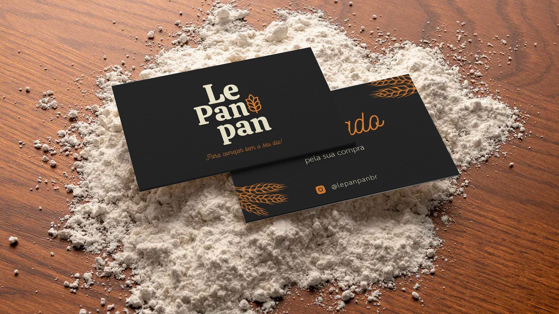 Dois cartões de visita estão em cima de uma pilha de farinha sobre uma mesa de madeira.