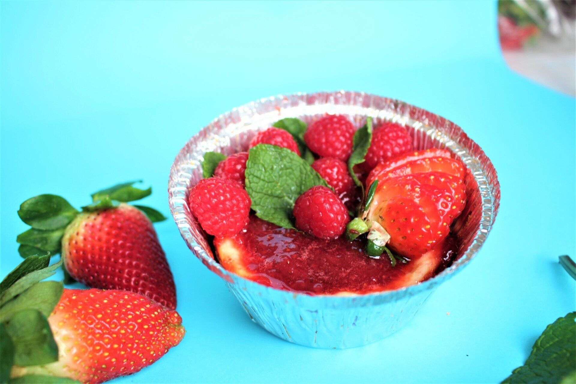 Uma tigela de cheesecake com framboesas e morangos sobre um fundo azul.