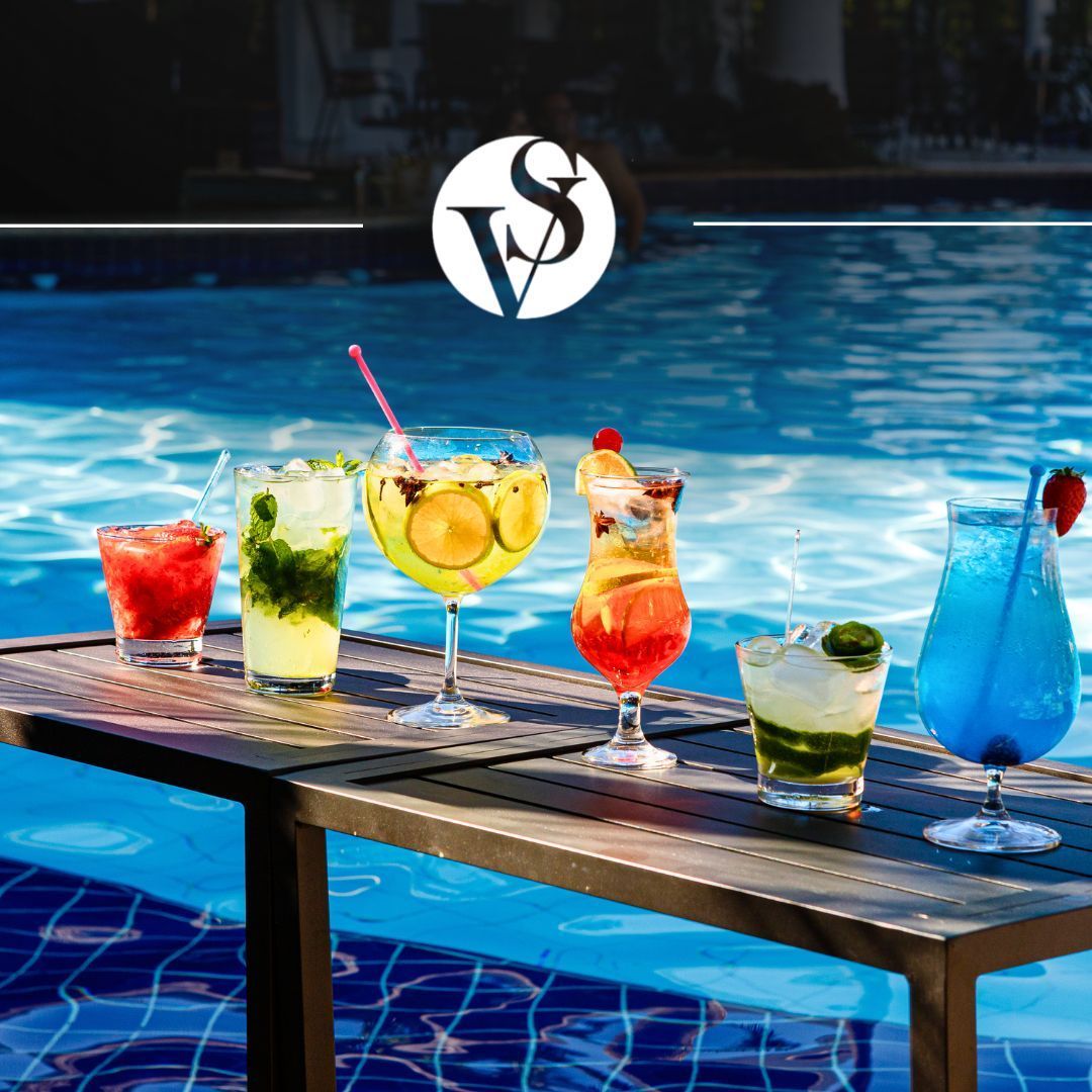 Ao fundo uma piscina e sobre uma mesa 6 bebidas diferentes