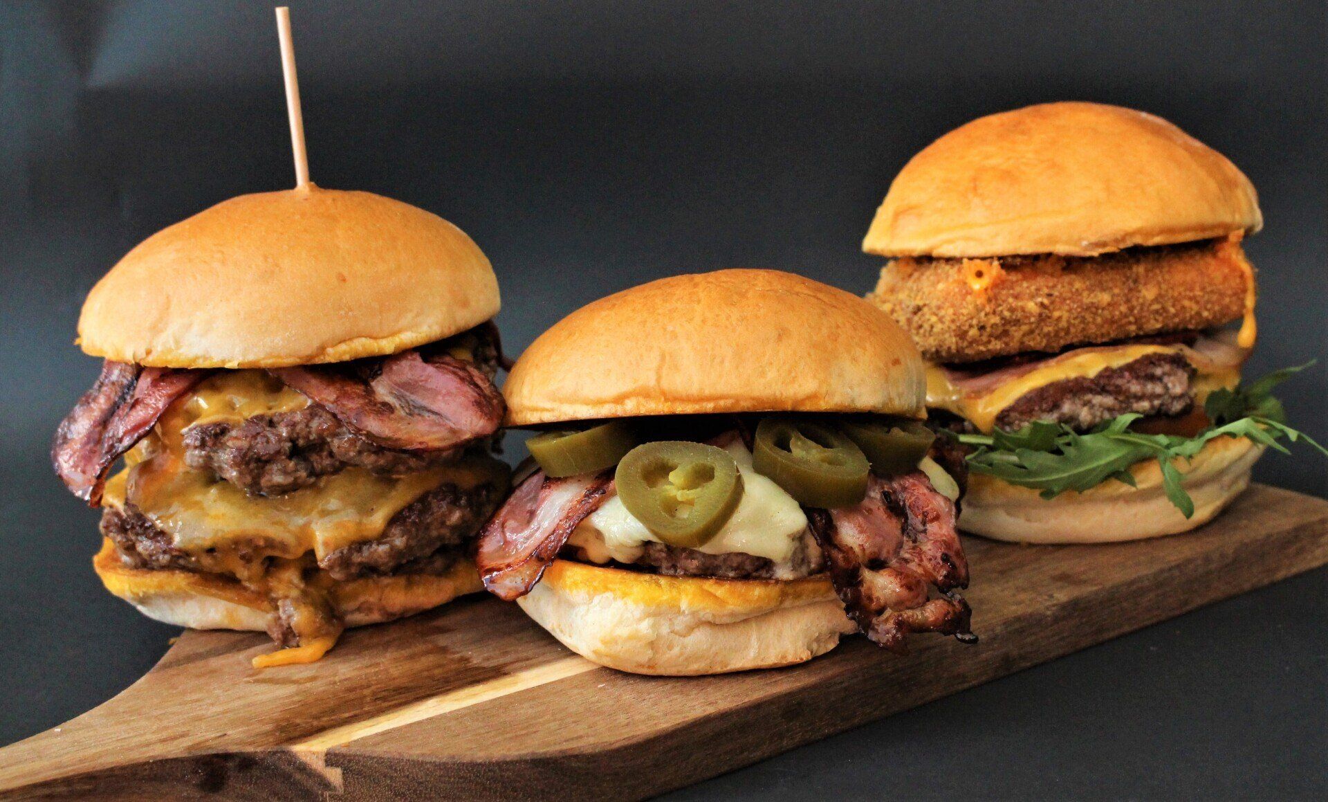 Três hambúrgueres estão sobre uma tábua de madeira.