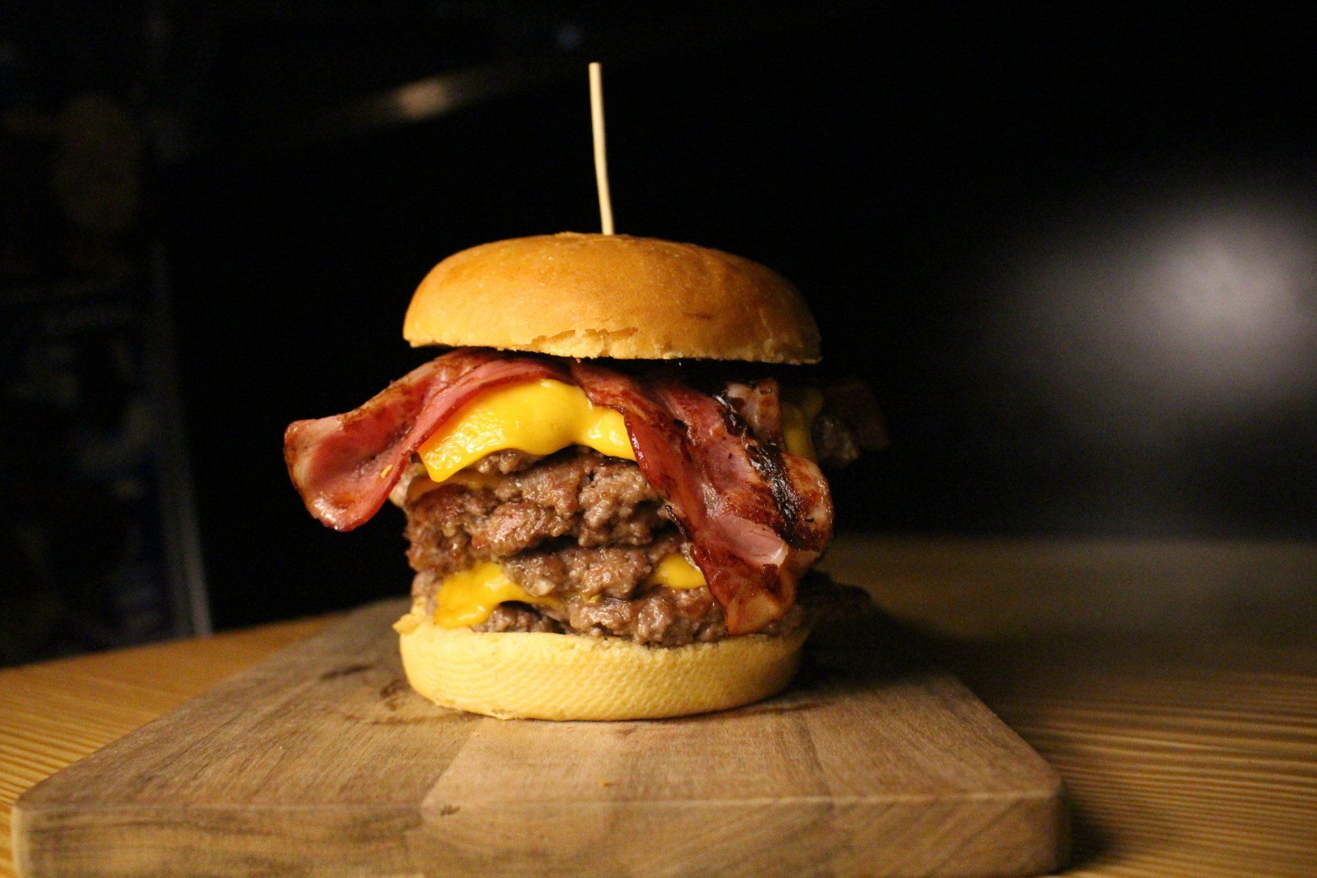 Um cheeseburger duplo com bacon em uma tábua de madeira.