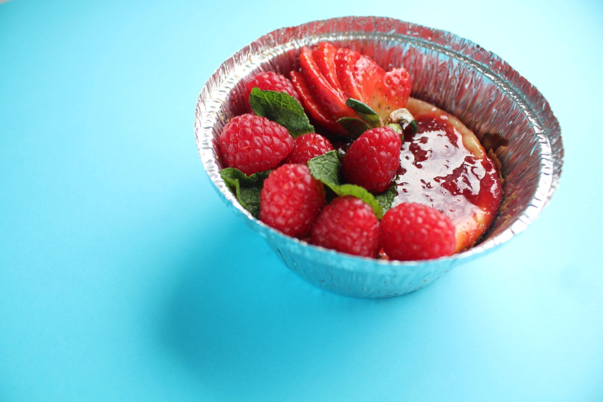 Uma tigela de framboesas e morangos sobre uma superfície azul.