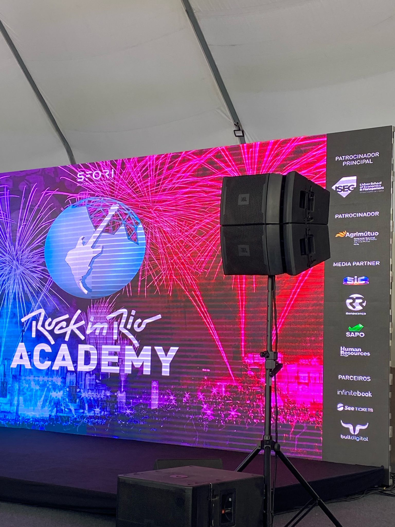 Um palco com alto-falantes e um grande telão atrás dele.