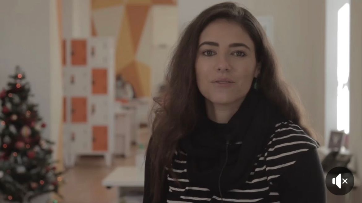 Uma mulher com uma camisa listrada preta e branca está em frente a uma árvore de natal.