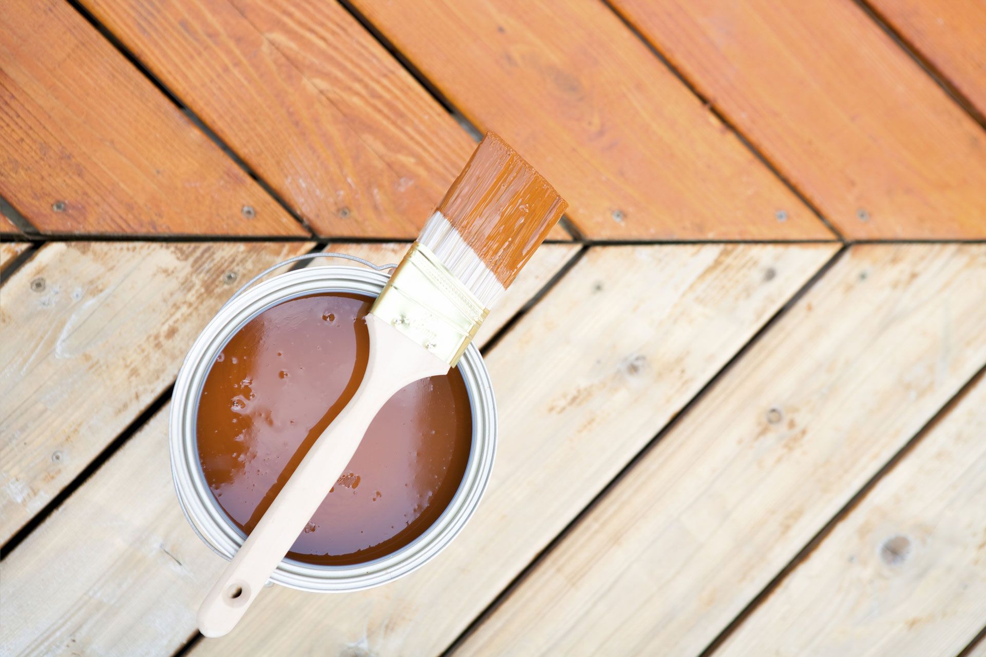 A can of wood stain and a brush on a wooden deck.