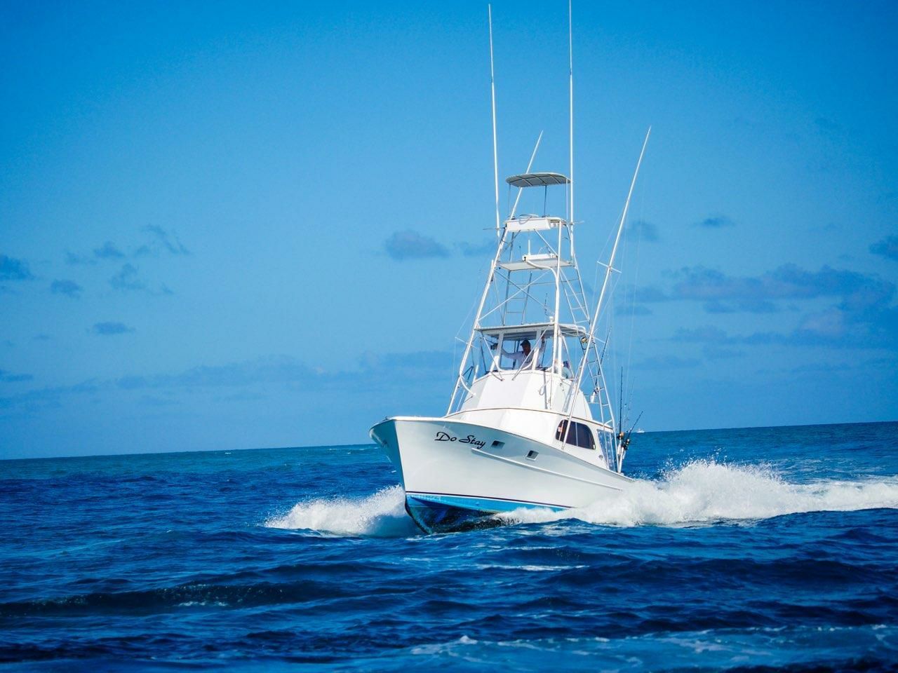 A white sport fishing boat cruising through deep blue ocean waves under a clear sky.