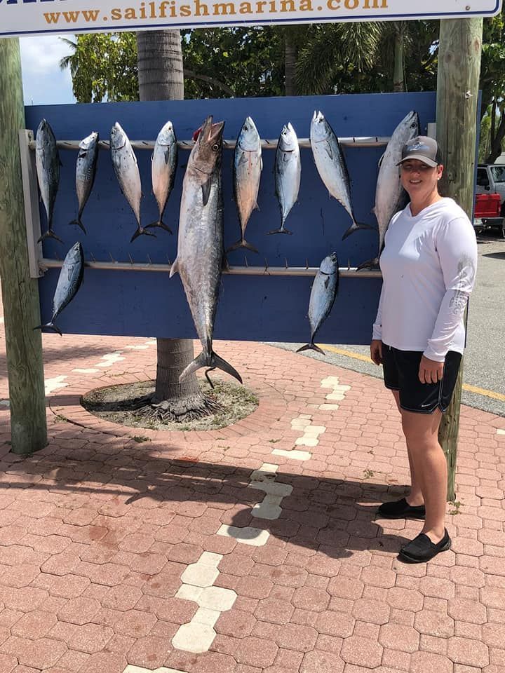 A person standing beside a blue marina display board featuring a large catch of multiple fish hung on hooks.