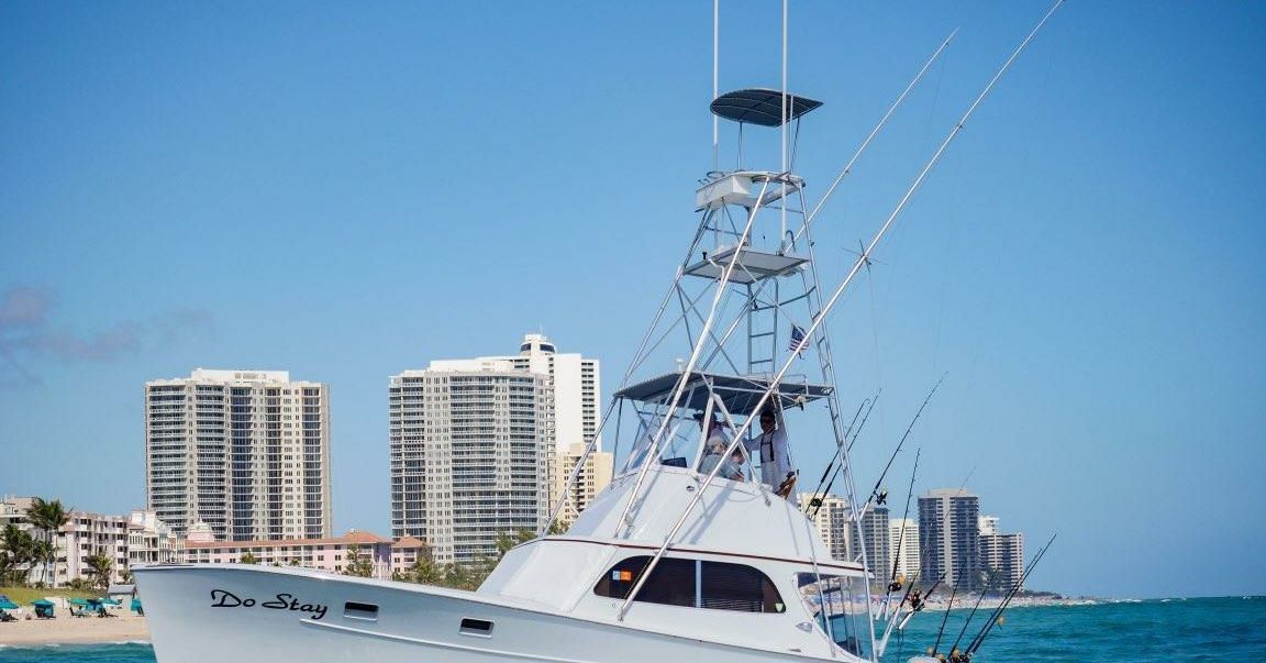 A white sport fishing boat cruises on turquoise water in front of a shoreline with large apartment buildings.