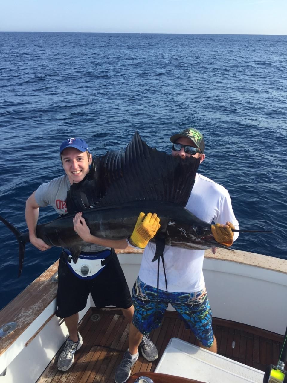 Two people holding a large sailfish on the deck of a boat at sea.