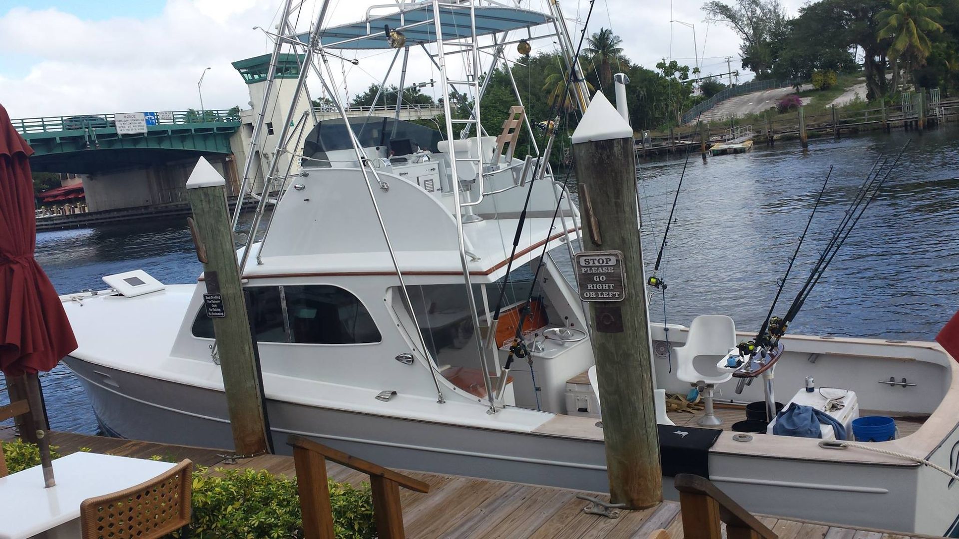 A white sport fishing boat moored at a dock, with a drawbridge visible in the background over the water.