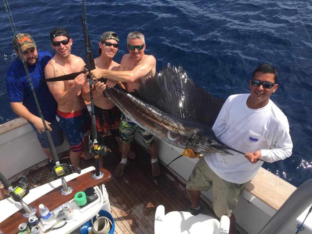 Five people on a fishing boat deck hold a large sailfish, which they have caught in the open ocean.