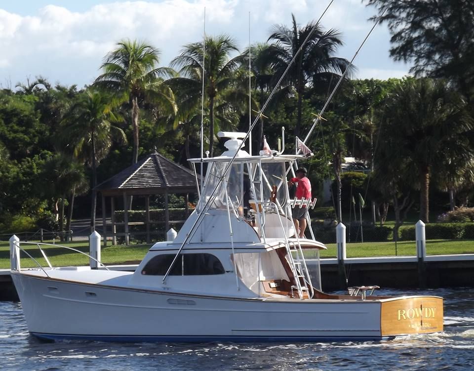 A white sport fishing boat cruises along a canal lined with palm trees and a wooden gazebo.