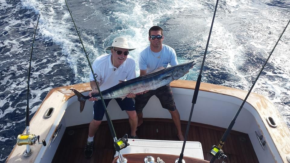 Two people hold a wahoo fish on the back of a boat while out at sea.