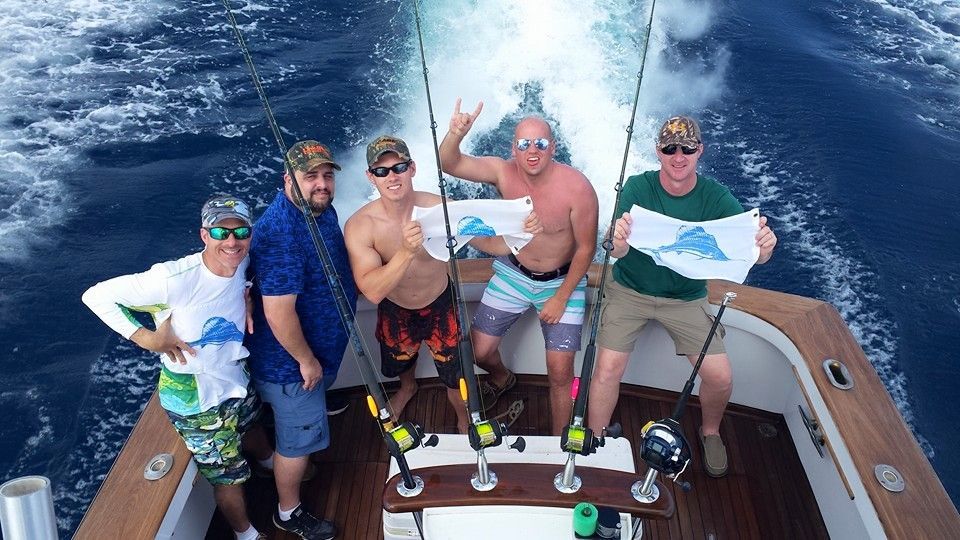 Five people stand on a boat deck holding flags in the open ocean.