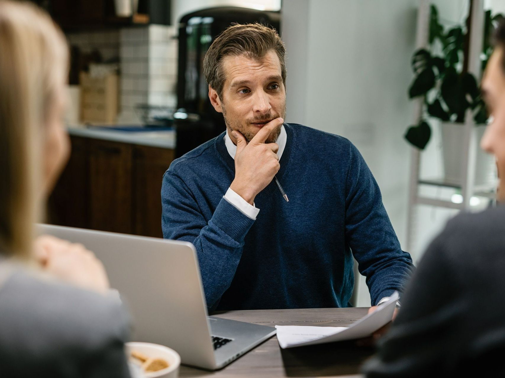 A man is sitting at a table with a laptop and a pen in his hand.