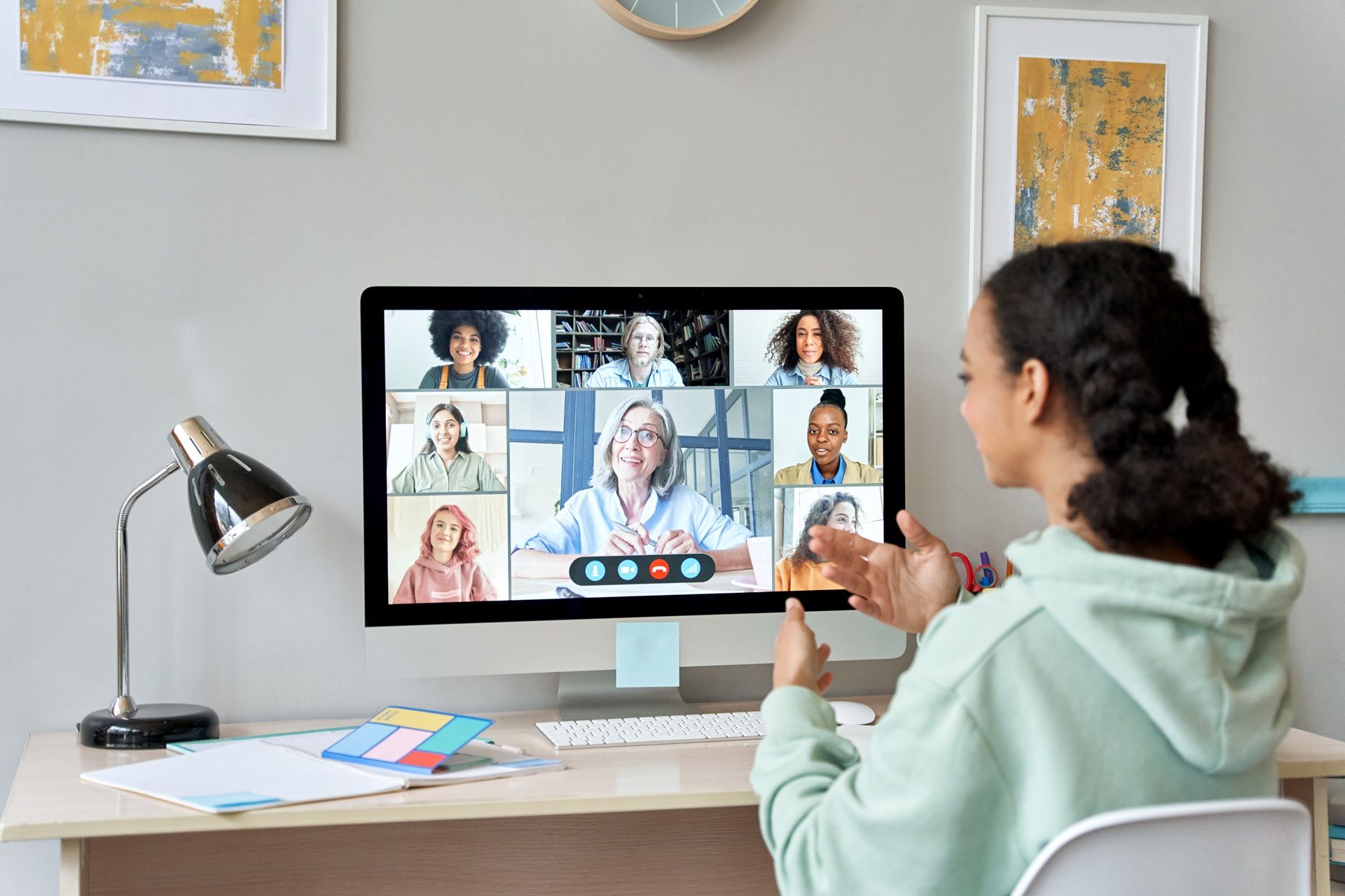 A woman is sitting at a desk using a computer to have a video call with a group of people.