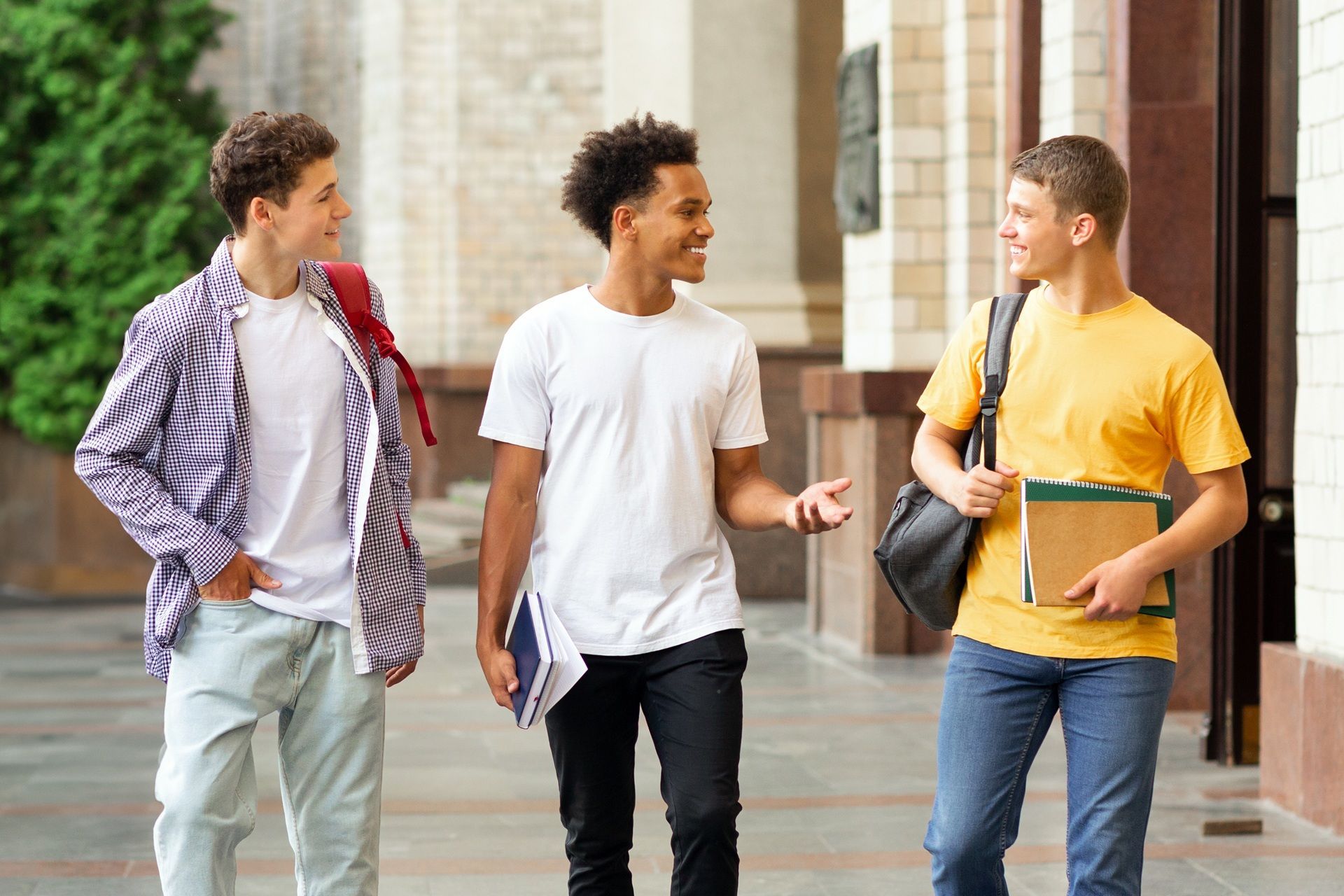 Three young men are walking down the street and talking to each other.