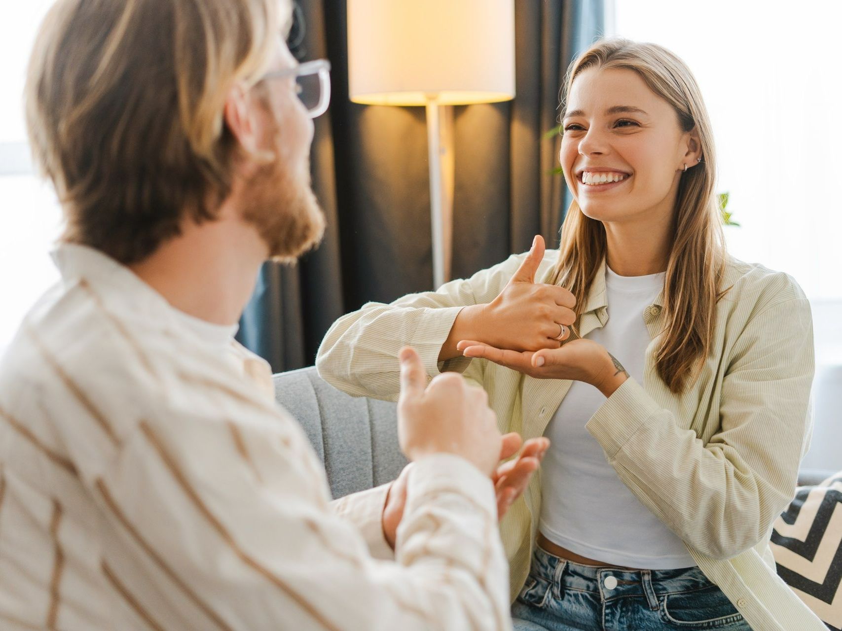 A man and a woman are sitting on a couch talking to each other in sign language.