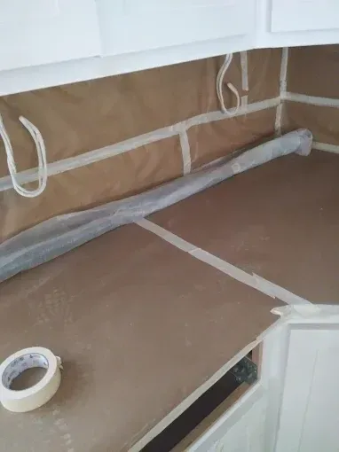 Countertop covered in brown paper and tape, prepared for painting in a kitchen.