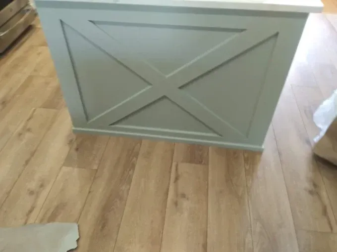Gray wooden cabinet with an X design on a light wood floor.