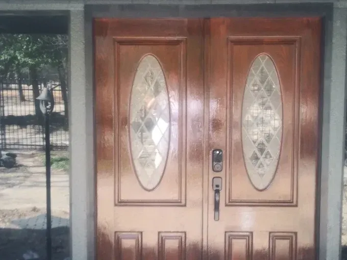 Wooden double doors with oval glass panels and a lock, outdoors.