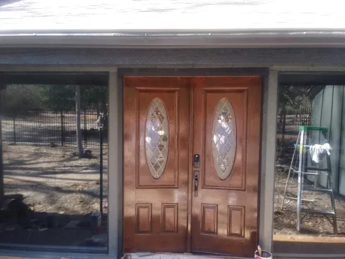 Double brown wooden doors with oval glass panels; flanked by tinted windows.