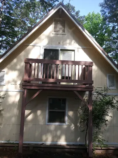 Tan two-story cabin with a balcony, a window below the balcony, and a gable roof.