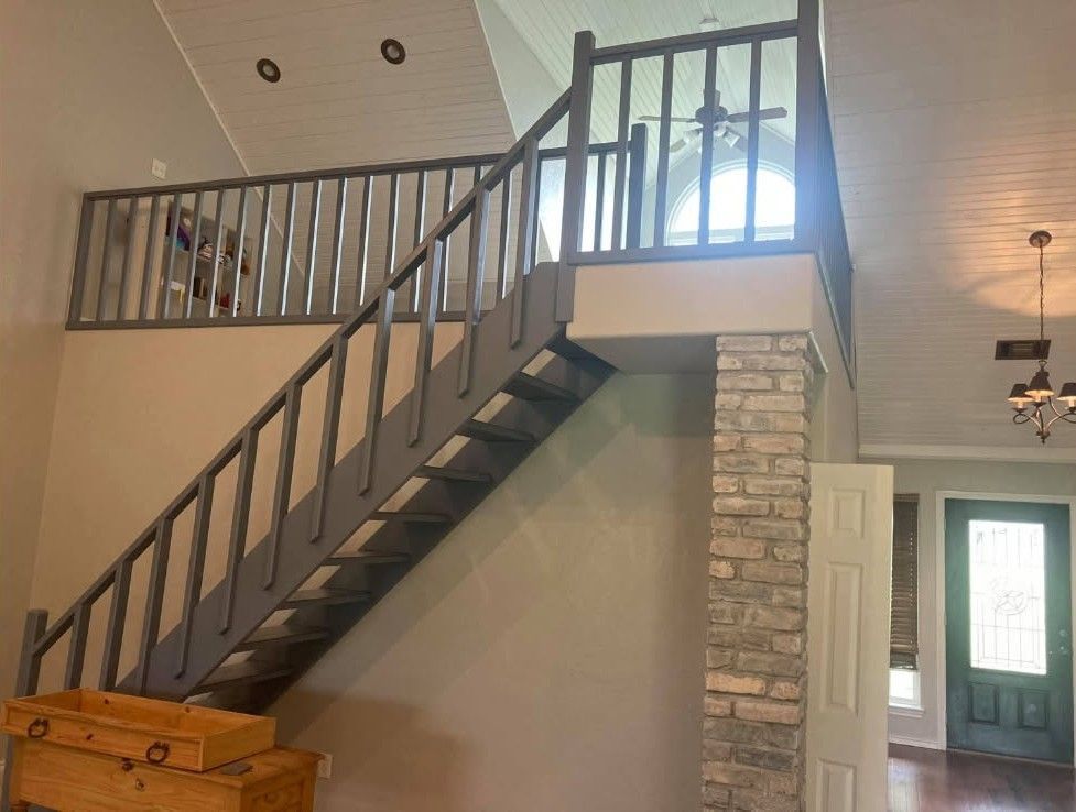 Interior view of a gray staircase leading to a loft with gray railings; brick support and a door are visible.