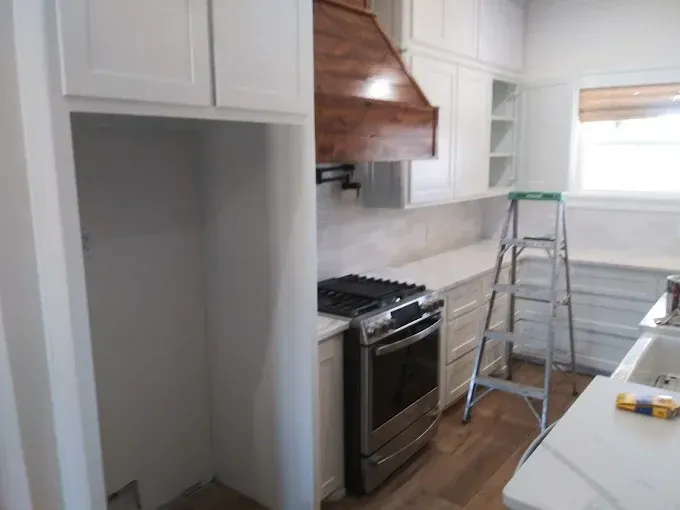 Kitchen with white cabinets, stainless steel oven, and brown vent hood. Ladder sits by the countertop.