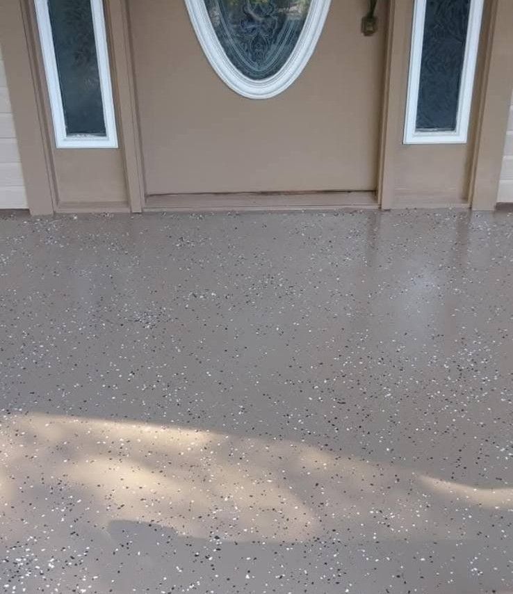 Brown speckled epoxy-coated concrete porch in front of a tan door with sidelight windows.