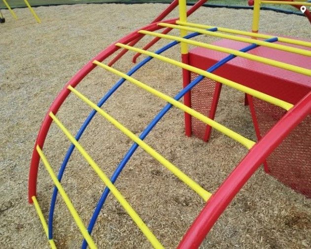 Red, yellow, and blue playground climber on wood chips.