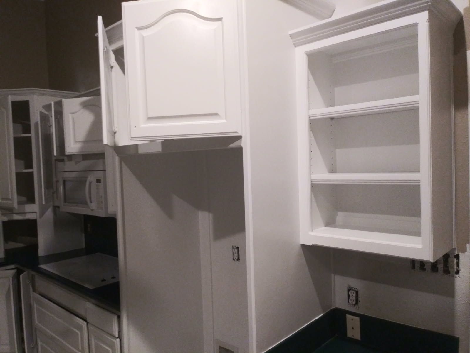 White kitchen cabinets with one open, next to a small shelf unit.
