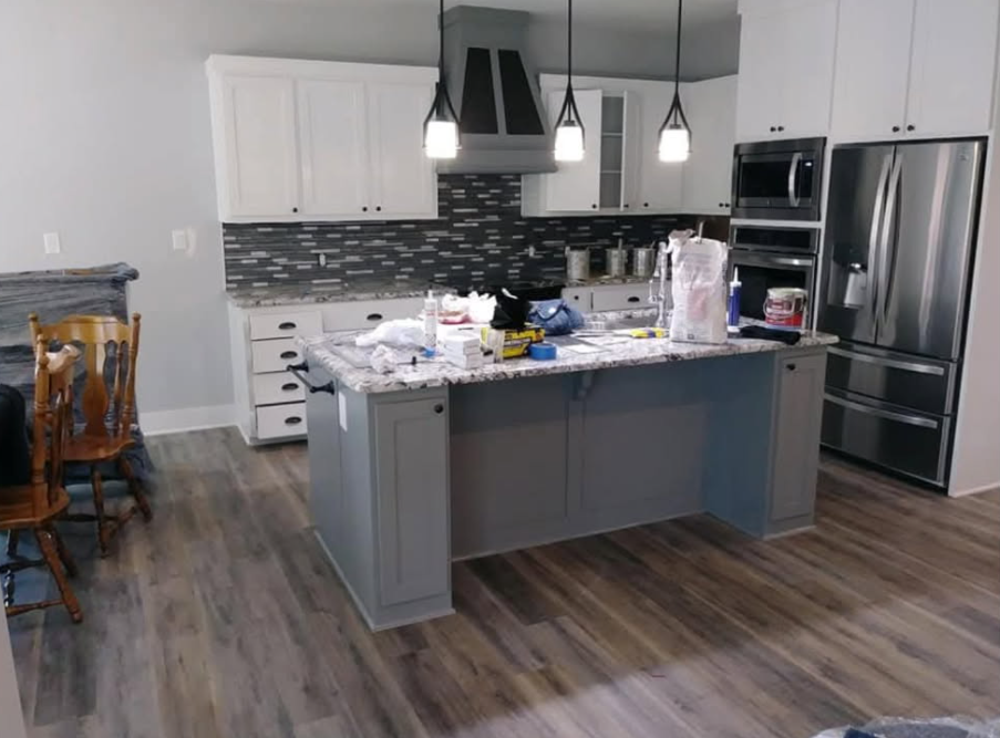 Modern kitchen with grey island, white cabinets, stainless steel appliances, and grey and white backsplash.