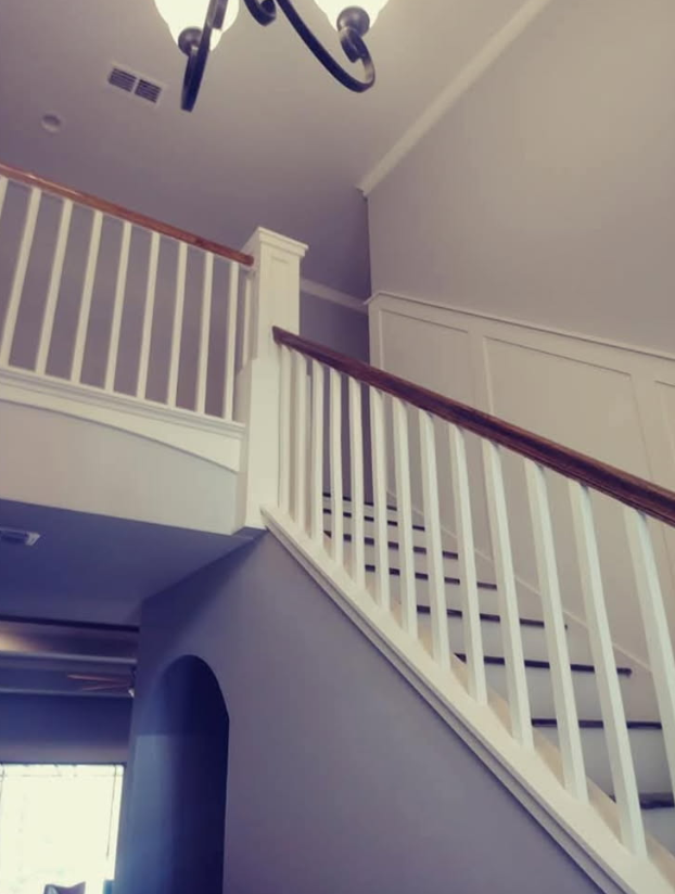 Staircase with white railings, brown handrails, and gray walls; chandelier visible above.