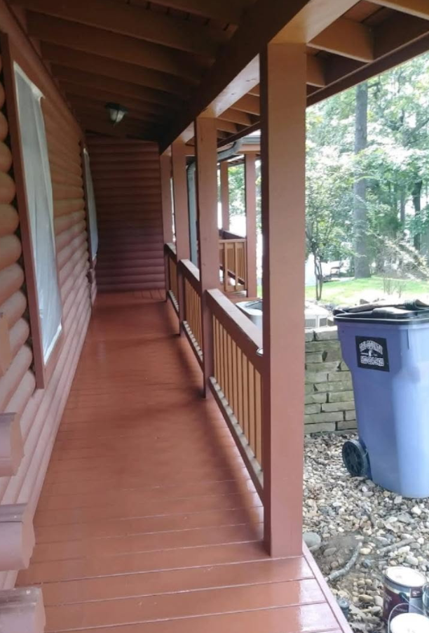 Wooden porch with reddish-brown paint, railing, and posts. A blue trash can sits nearby.