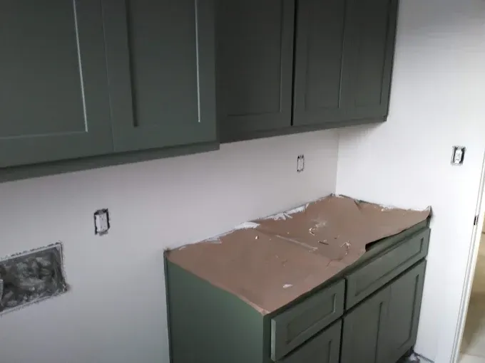 Green kitchen cabinets installed against white walls.