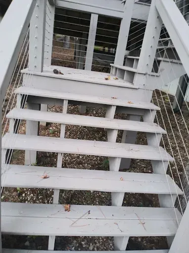 Gray wooden outdoor staircase with cable railings, descending into a yard.