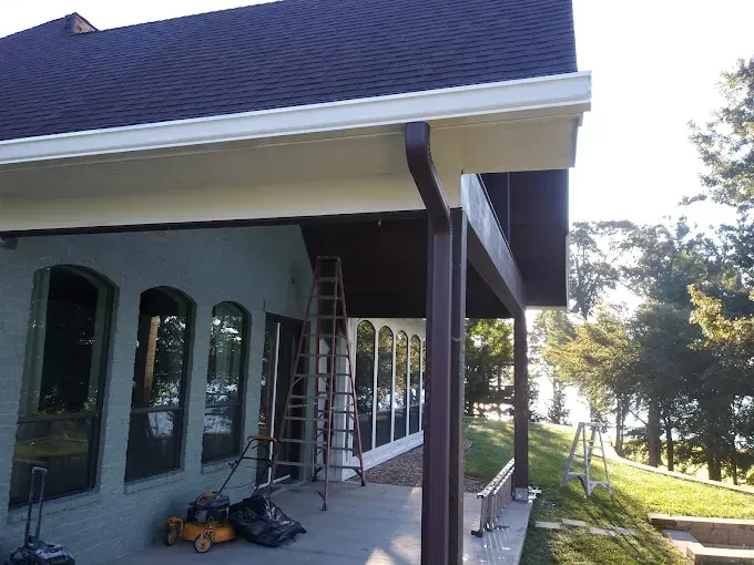 A home with brown roof, white gutters, and a porch. A ladder stands near the window.
