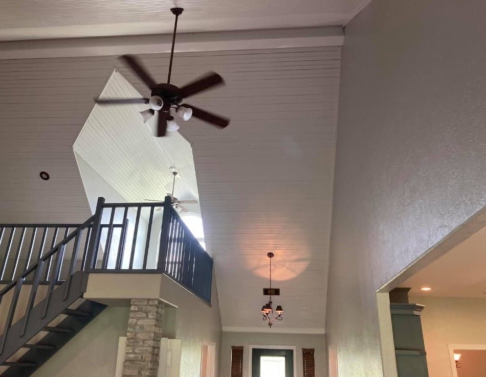 High-ceilinged interior with ceiling fans, staircase, and a gray wall.