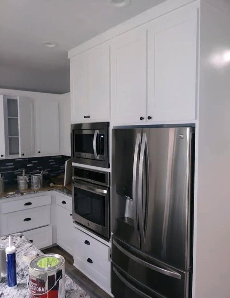 White kitchen cabinets surround a stainless steel refrigerator and built-in microwave and oven.