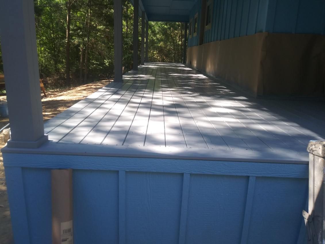 Blue porch with white-painted wooden floor, trees in the background.