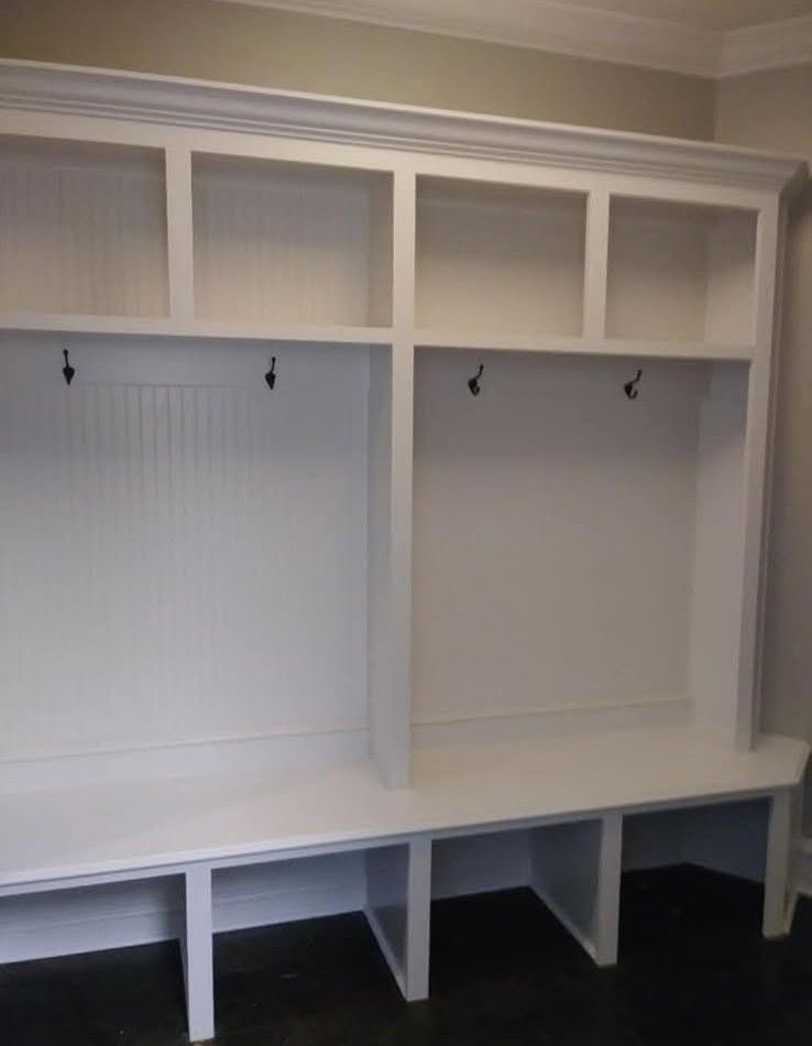 White built-in storage unit with coat hooks, bench seating, and open shelving.