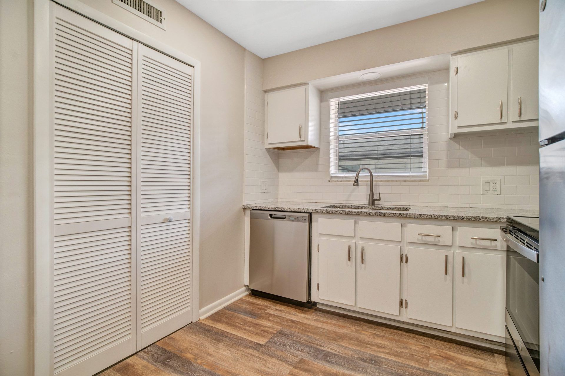 A kitchen with white cabinets , stainless steel appliances , and a window.