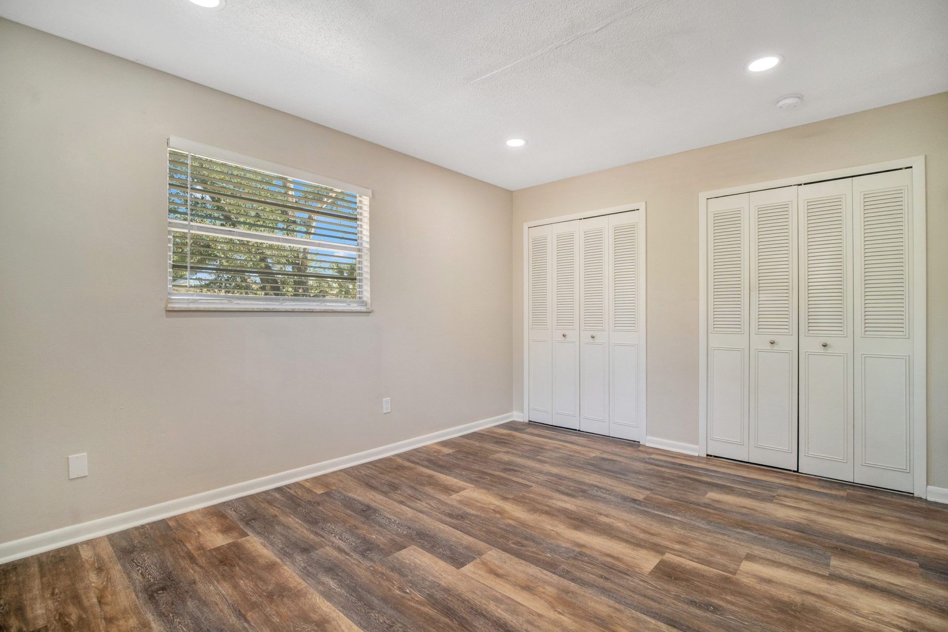 An empty room with hardwood floors and white closet doors.