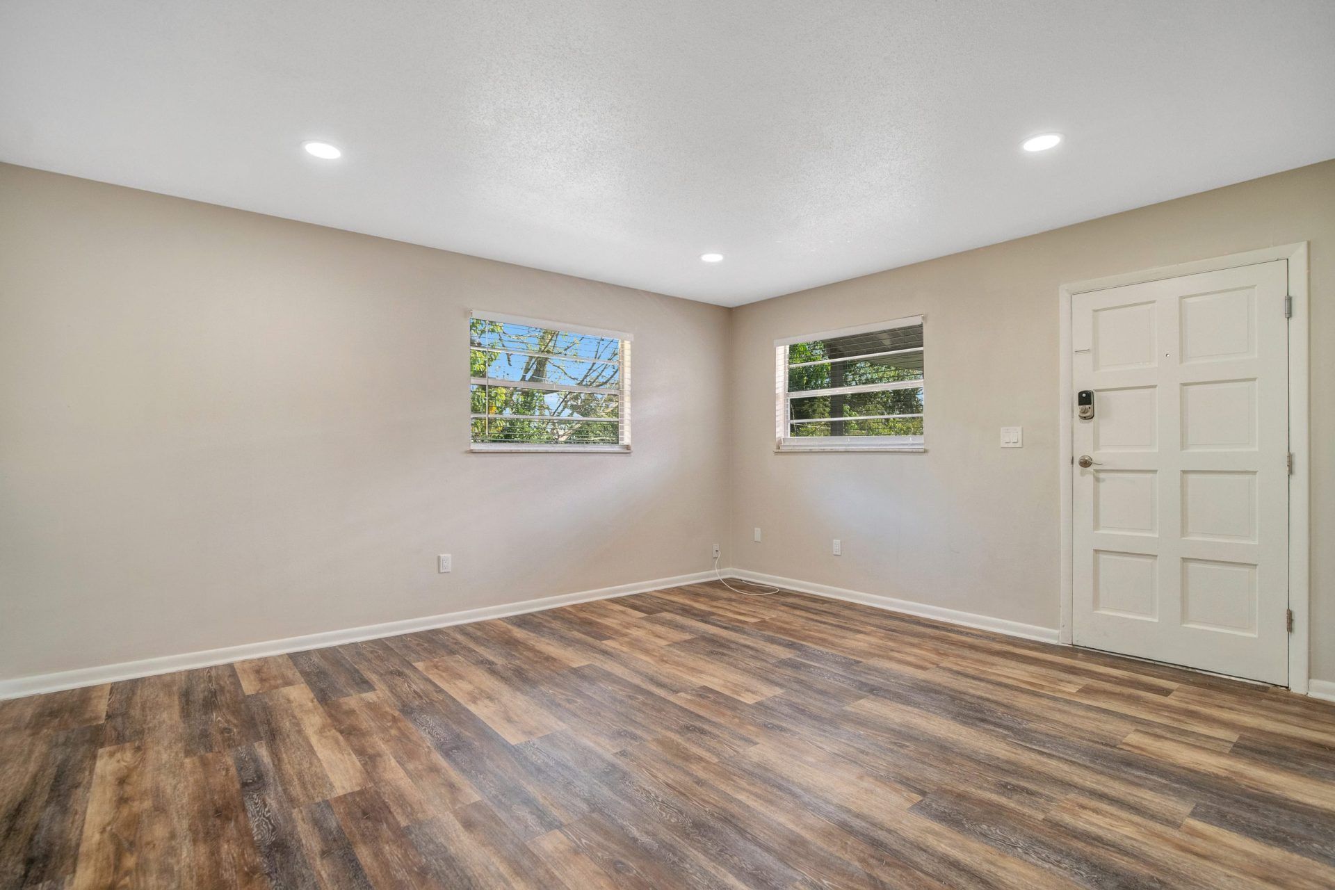 An empty living room with hardwood floors and two windows.