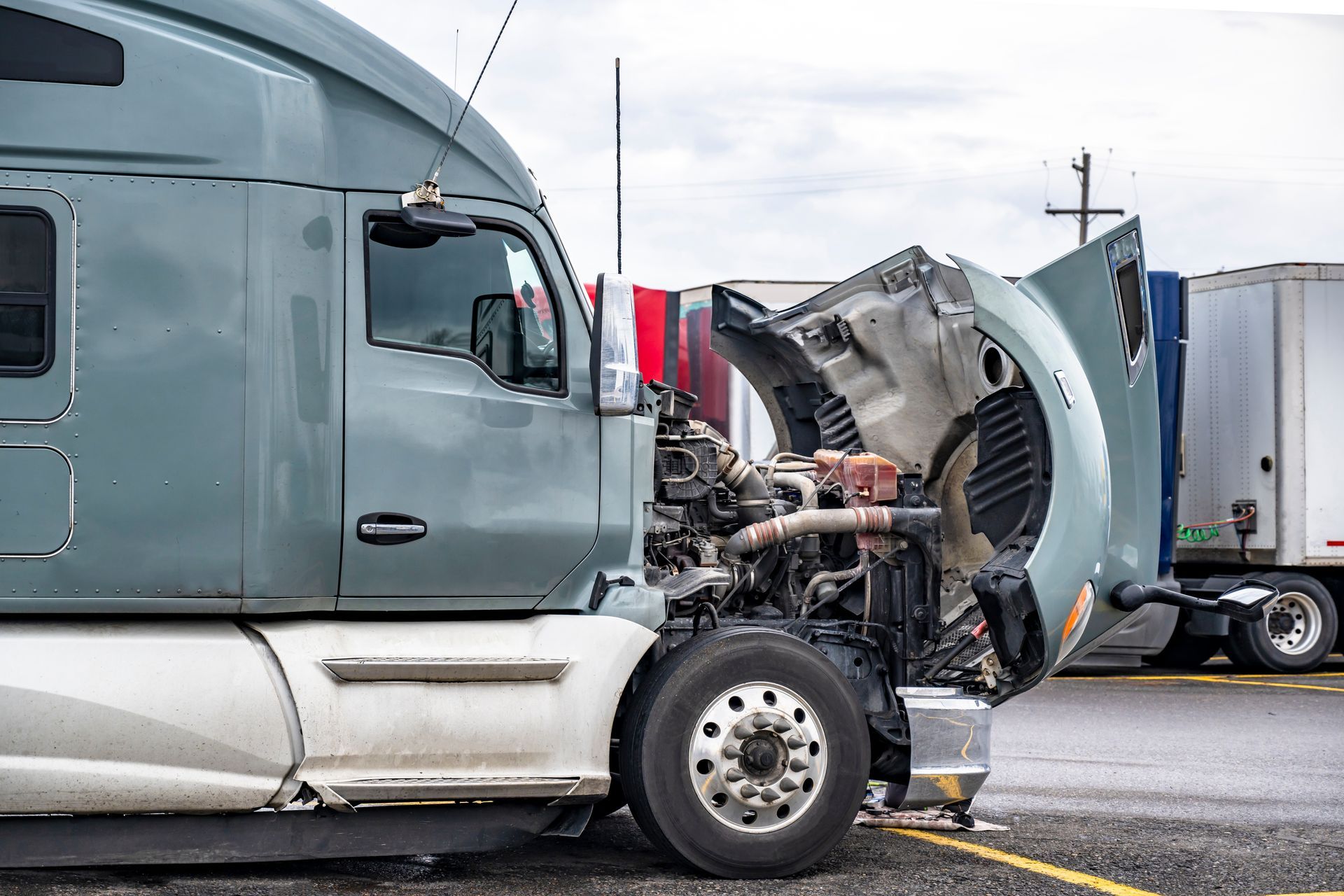 Parked semi truck with hood raised, showing engine exposed for roadside repair work.