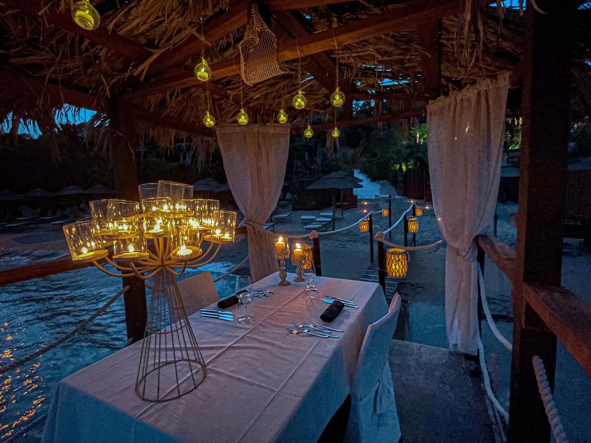 Un tavolo con delle candele è appoggiato accanto a uno specchio d'acqua.