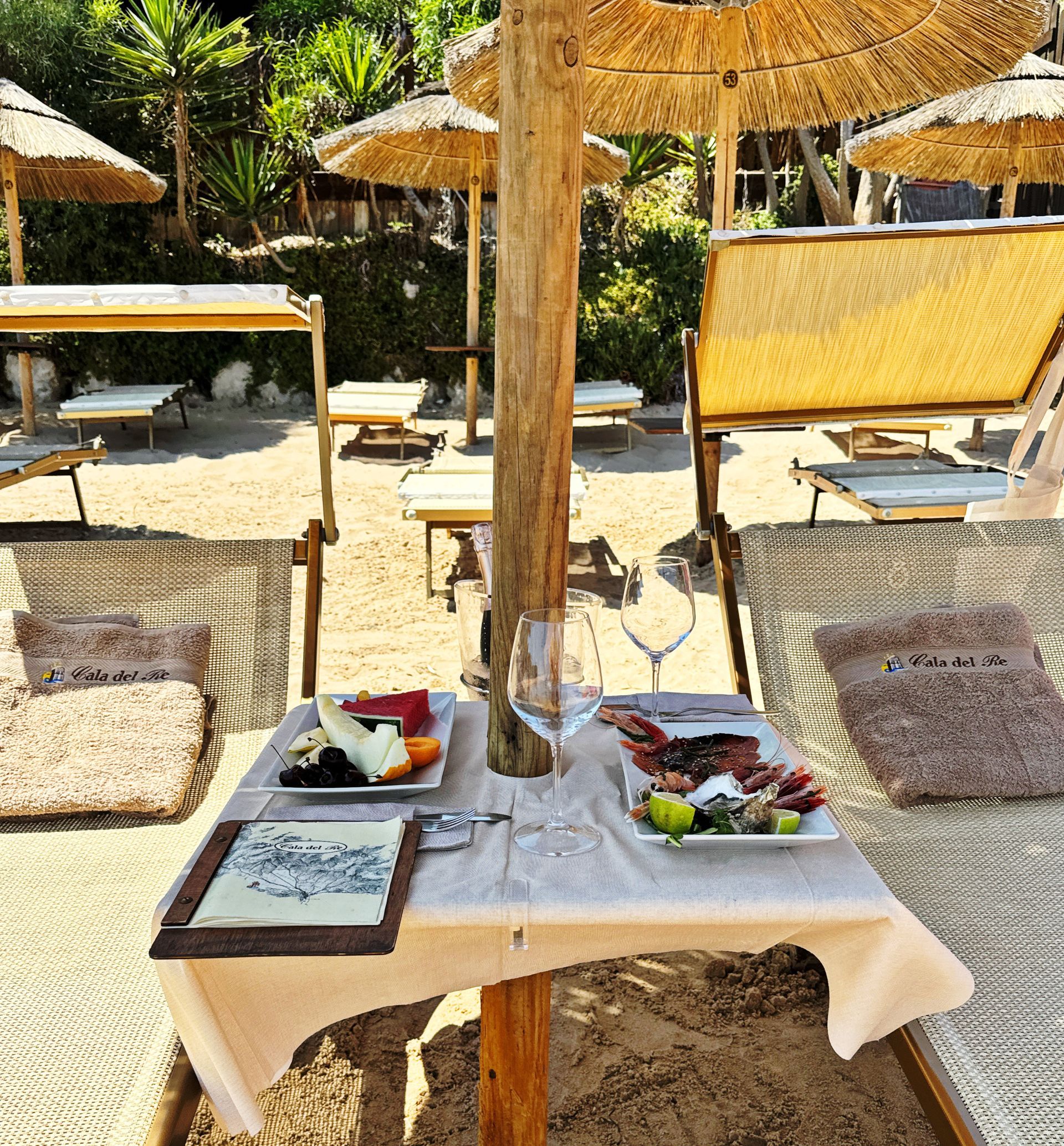Un tavolo con piatti di cibo e un bicchiere di vino sotto un ombrellone in spiaggia